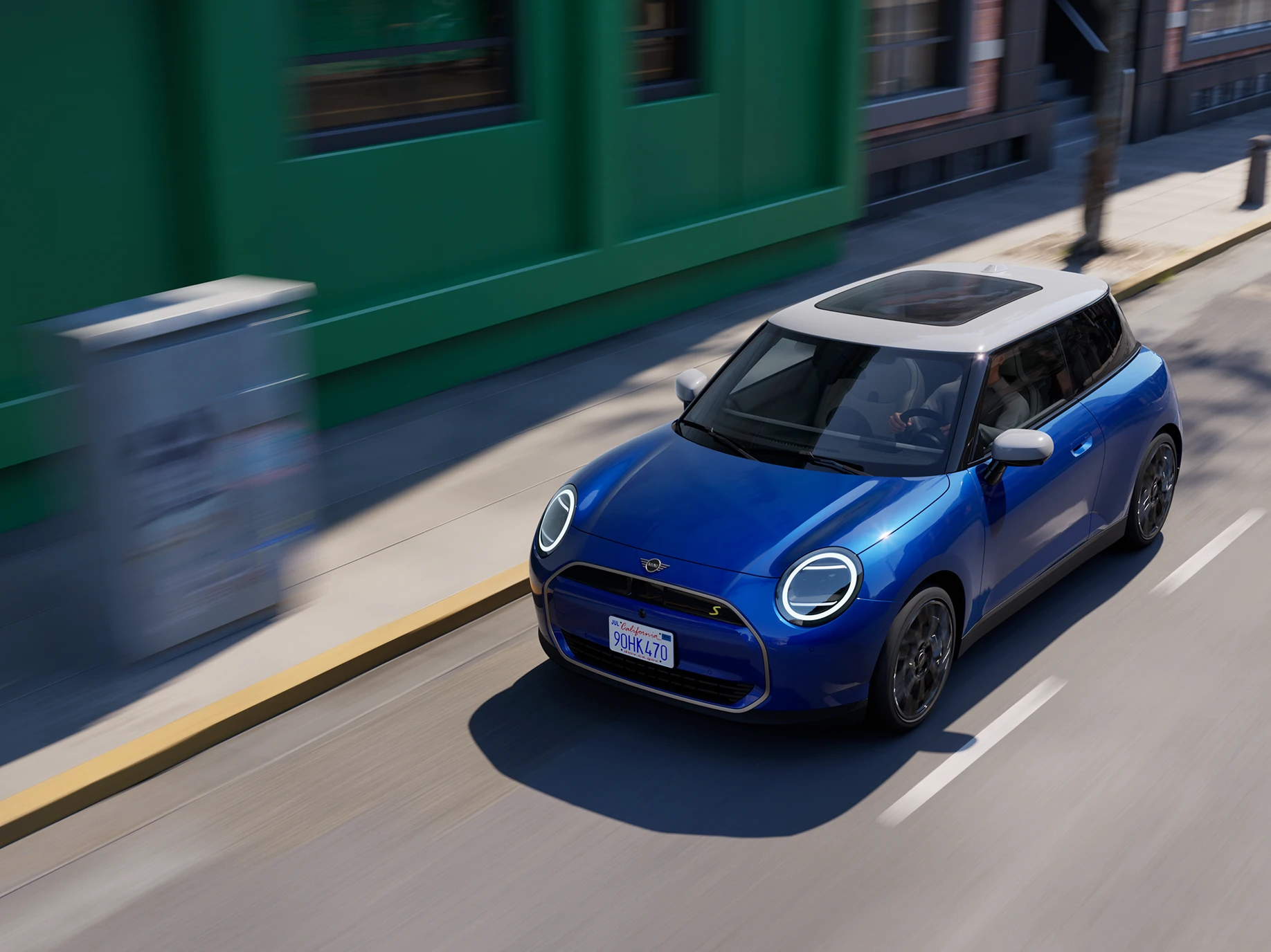 Täiselektriline Blazing Blue värvitoonis ja valge katusega MINI Cooper tänaval sõitmas, ülaltvaade.