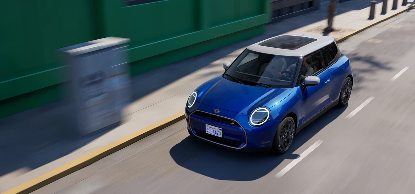 Täiselektriline Blazing Blue värvitoonis ja valge katusega MINI Cooper tänaval sõitmas, ülaltvaade.