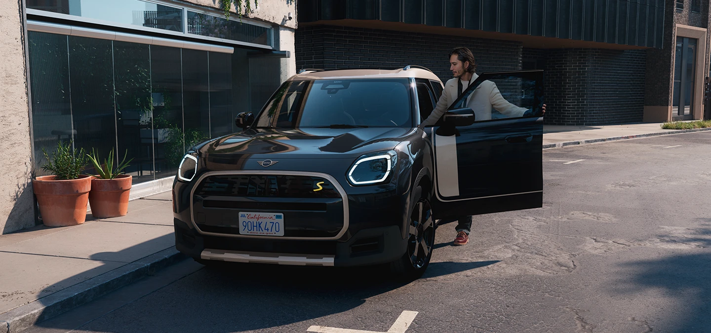 Midnight Blacki värvitoonis ja Vibrant Silveri katusega täiselektriline MINI Countryman tänaval, eestvaade.