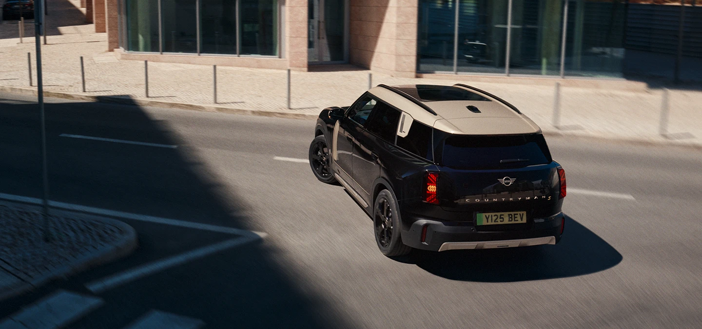 Midnight Blacki värvitoonis ja Vibrant Silveri katusega täiselektriline MINI Countryman parkimas, ülalt tagantvaade.