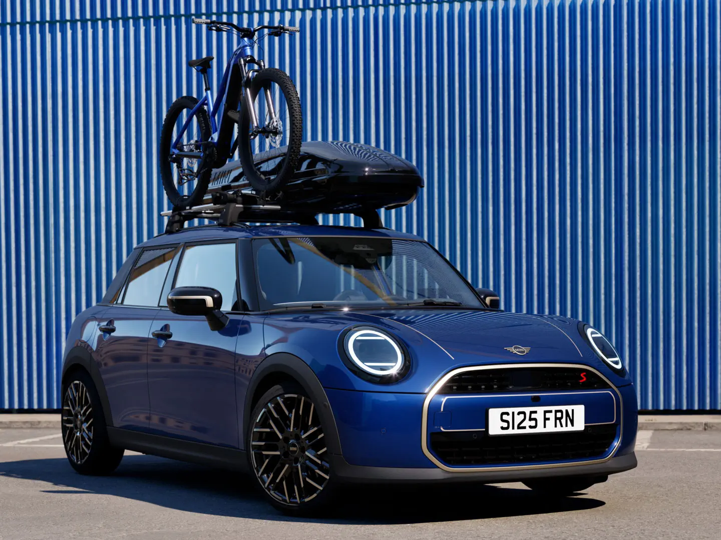 MINI Aceman esivaates värvitoonis Indigo Sunset Blue koos MINI katusele paigaldatava jalgrattahoidikuga, millel on maastikuratas, ja MINI katuseboksiga 320.