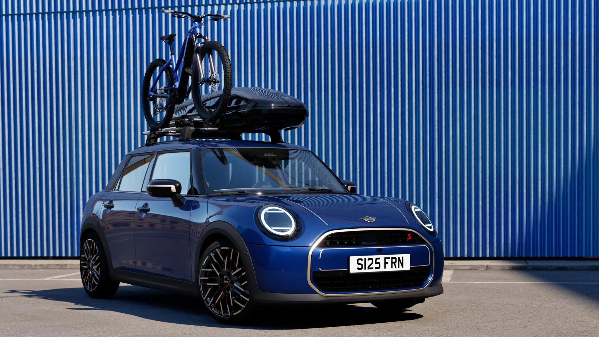 MINI Aceman esivaates värvitoonis Indigo Sunset Blue koos MINI katusele paigaldatava jalgrattahoidikuga, millel on maastikuratas, ja MINI katuseboksiga 320.