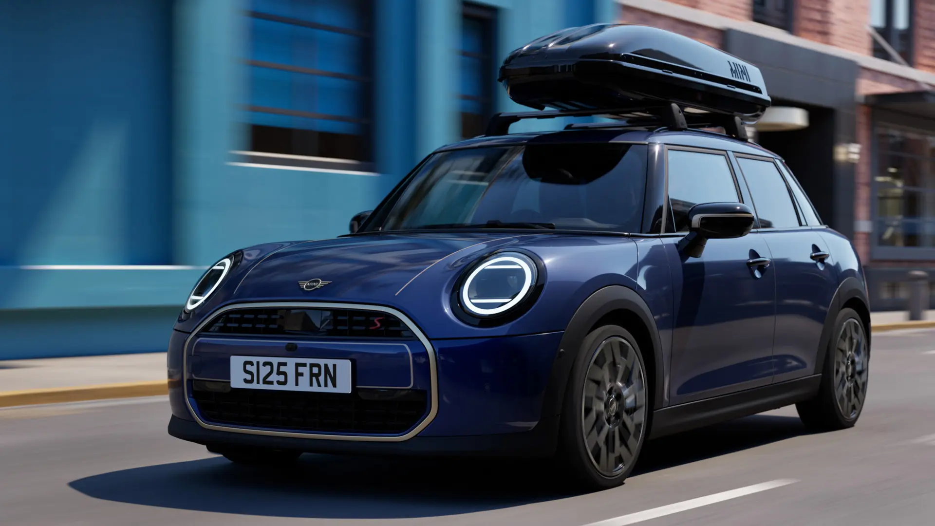 MINI Aceman kolmveerand eestvaates värvitoonis Indigo Sunset Blue, varustatud MINI katuseraamiga, millel on MINI katuseboks 320.