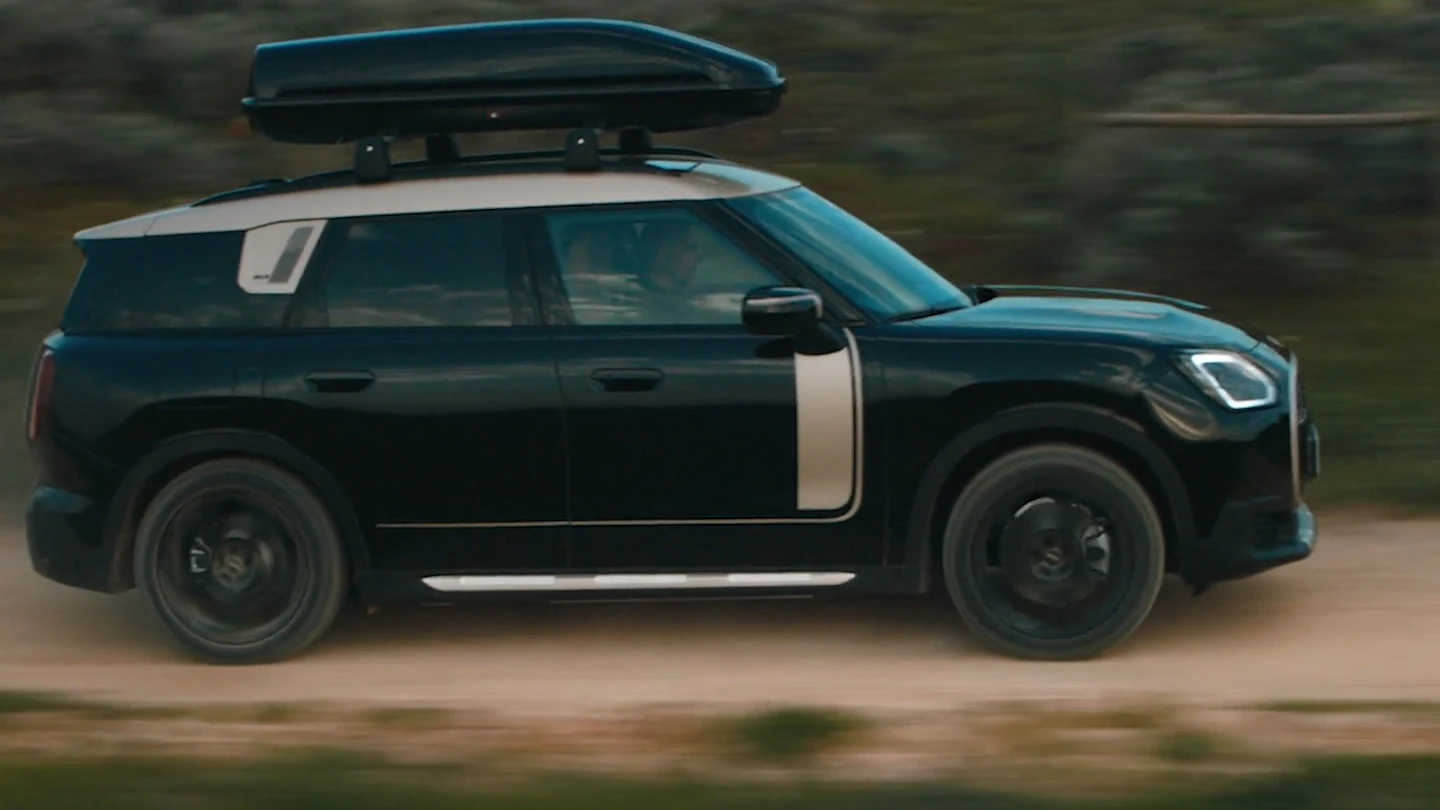 MINI Countryman värvitoonis Midnight Black metallik 19-tolliste mustade John Cooper Works Runway Spoke velgedega, maastikul sõitmas.